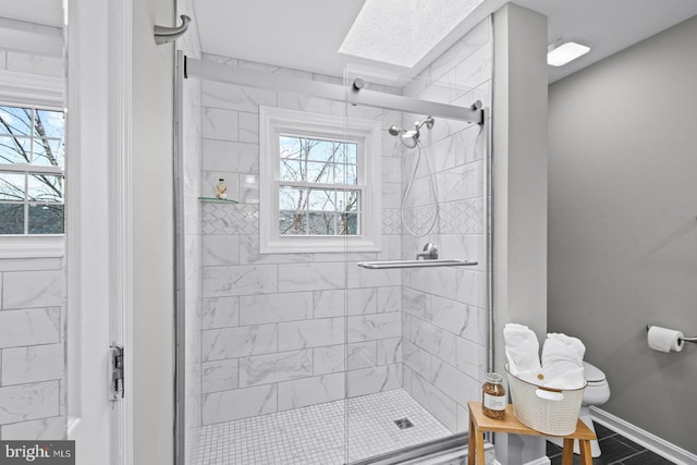 bathroom featuring a skylight, baseboards, toilet, and a stall shower