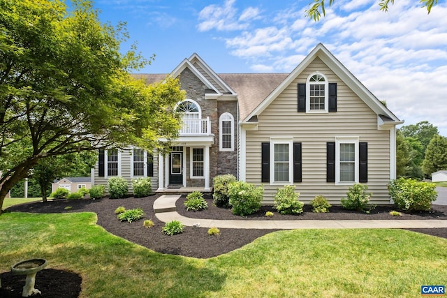 view of front facade featuring stone siding, a balcony, and a front lawn