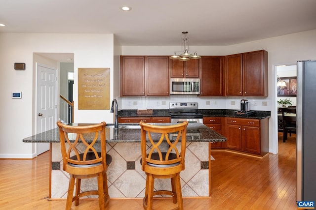 kitchen with a kitchen island with sink, a sink, hanging light fixtures, appliances with stainless steel finishes, and a kitchen bar