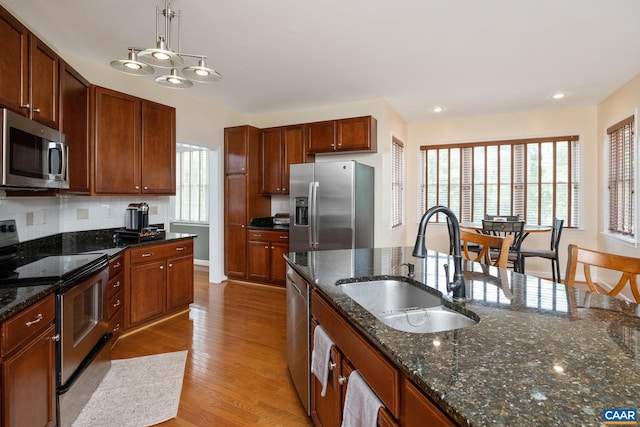 kitchen with appliances with stainless steel finishes, dark stone countertops, hanging light fixtures, and a sink