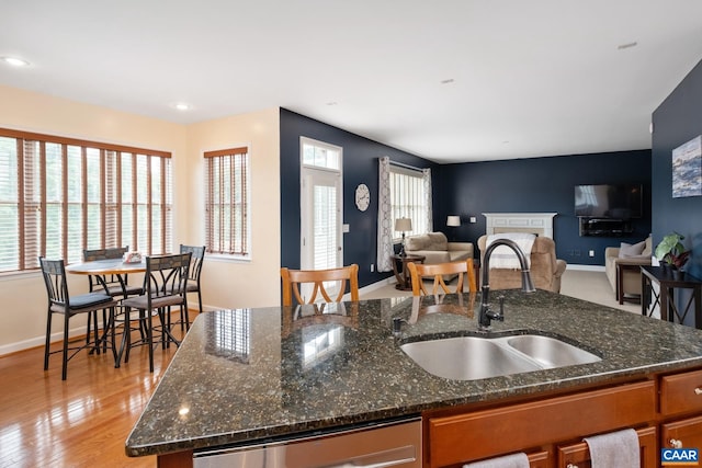 kitchen featuring open floor plan, a sink, dark stone countertops, an island with sink, and dishwasher