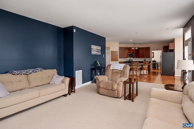 living area with light wood finished floors, visible vents, and baseboards