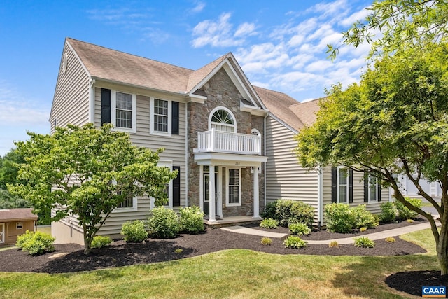 view of front of house featuring stone siding, a front lawn, roof with shingles, and a balcony