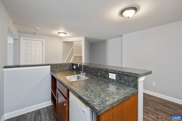 kitchen featuring dark wood-style flooring, dark countertops, a sink, a peninsula, and baseboards