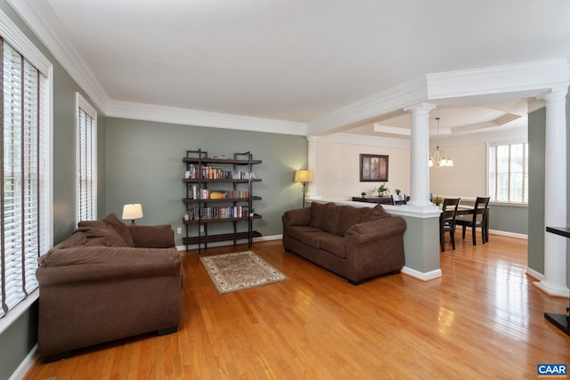 living area featuring light wood-style floors, decorative columns, crown molding, and an inviting chandelier