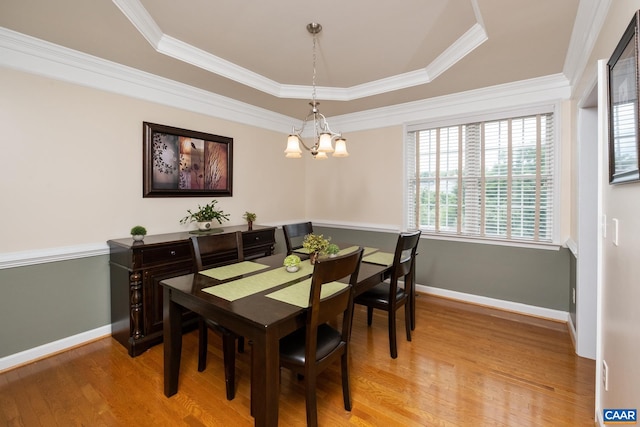 dining space with a notable chandelier, wood finished floors, baseboards, ornamental molding, and a raised ceiling