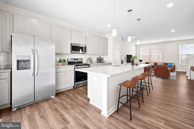 kitchen featuring stainless steel appliances, decorative light fixtures, light stone counters, and an island with sink