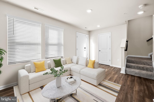 living room featuring dark wood-style floors, visible vents, baseboards, and stairs