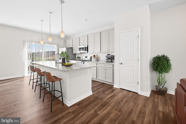 kitchen with an island with sink, appliances with stainless steel finishes, dark wood-style flooring, a kitchen bar, and pendant lighting