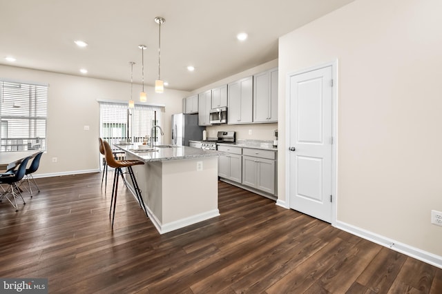 kitchen with hanging light fixtures, gray cabinetry, appliances with stainless steel finishes, an island with sink, and light stone countertops