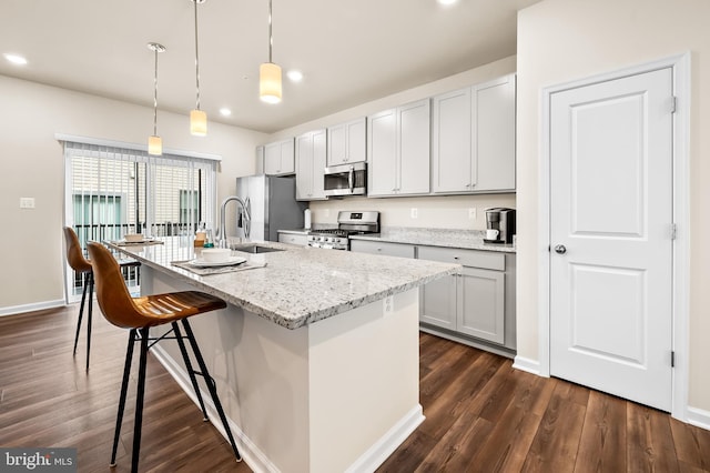 kitchen with an island with sink, pendant lighting, stainless steel appliances, and light stone counters