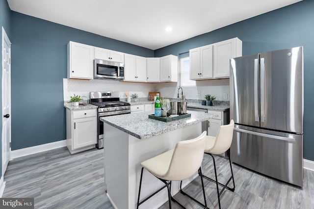 kitchen featuring a breakfast bar area, a center island, light stone countertops, stainless steel appliances, and white cabinetry