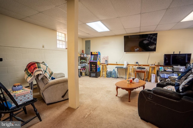 carpeted living room featuring a drop ceiling and concrete block wall