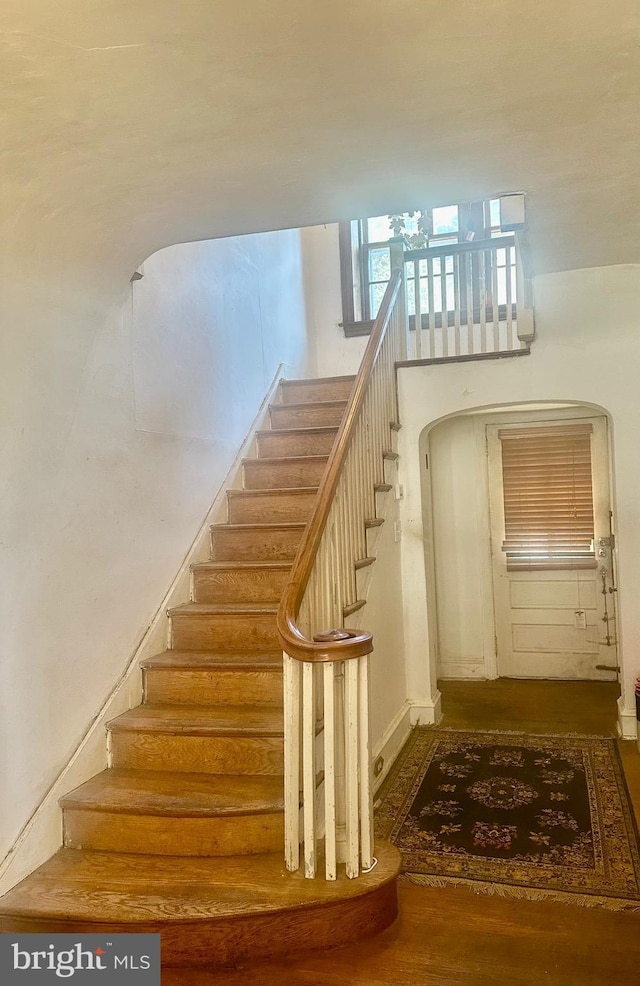 staircase featuring arched walkways and wood finished floors