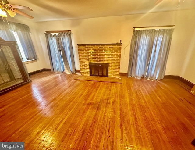 unfurnished living room with ceiling fan, a fireplace, baseboards, and wood finished floors