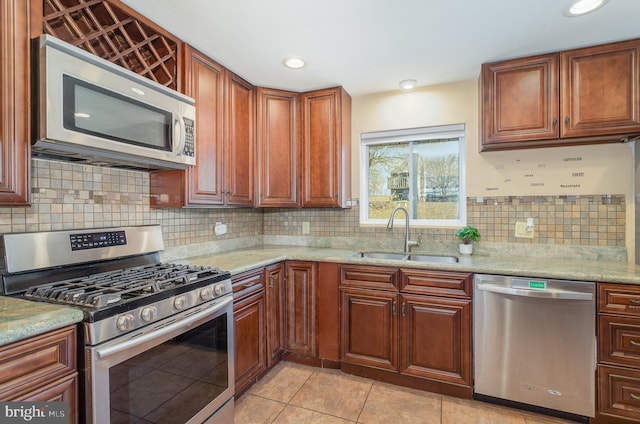 kitchen featuring light stone counters, brown cabinets, backsplash, appliances with stainless steel finishes, and a sink