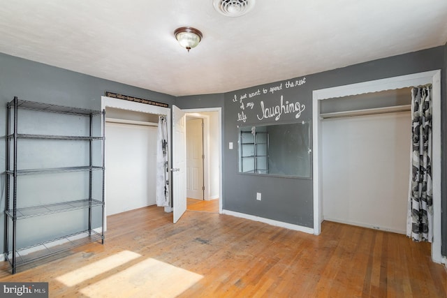 unfurnished bedroom featuring baseboards, a closet, visible vents, and wood finished floors