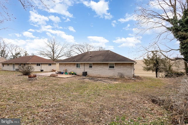 back of property with an outdoor fire pit, cooling unit, brick siding, a yard, and a patio area