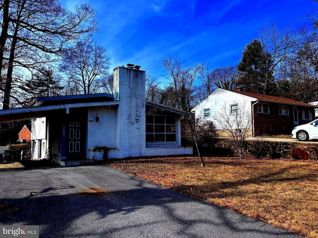 view of property exterior featuring a carport, brick siding, a chimney, and aphalt driveway