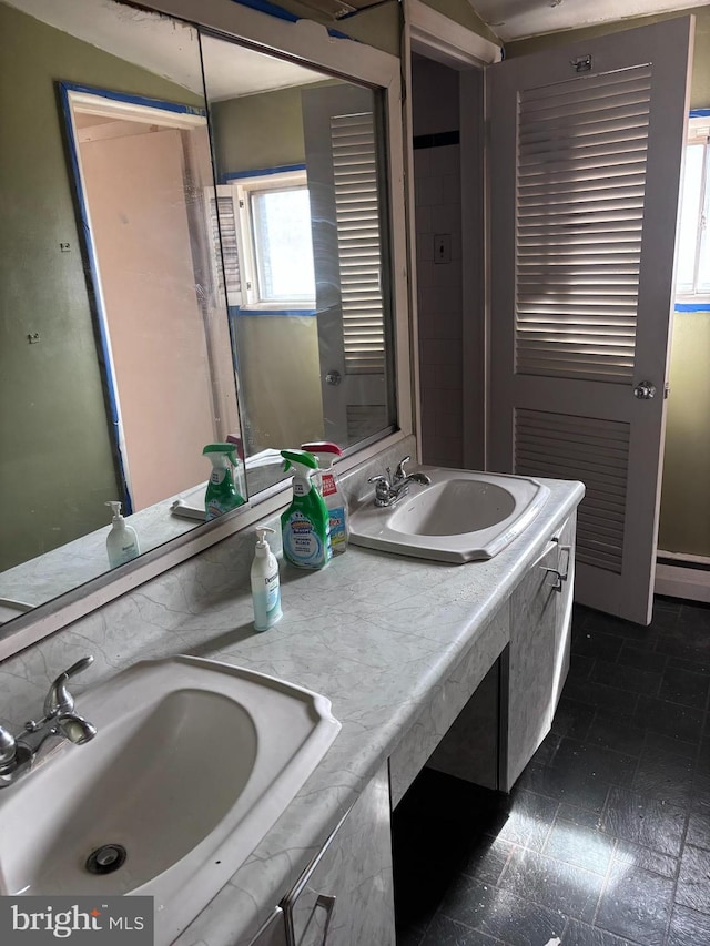 full bath with double vanity, baseboard heating, and a sink