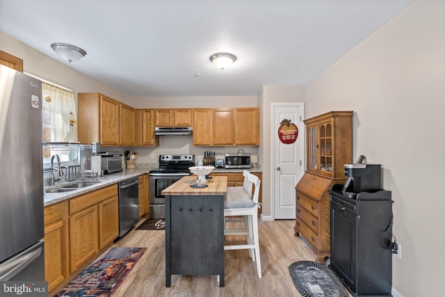 kitchen with a center island, stainless steel appliances, wood counters, under cabinet range hood, and a kitchen bar