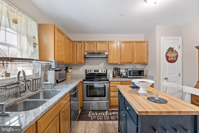 kitchen featuring under cabinet range hood, stainless steel appliances, a sink, wood finished floors, and wood counters