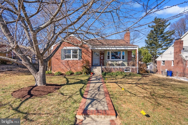 bungalow with a front yard, covered porch, brick siding, and a chimney