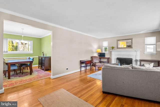 living area featuring baseboards, a fireplace, a notable chandelier, and light wood finished floors