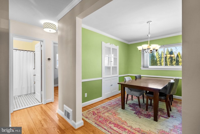 dining space with a notable chandelier, visible vents, baseboards, wood-type flooring, and crown molding