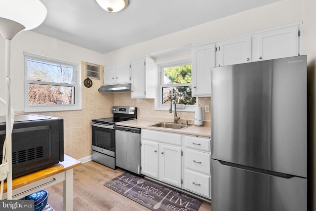 kitchen with white cabinets, appliances with stainless steel finishes, light countertops, under cabinet range hood, and a sink