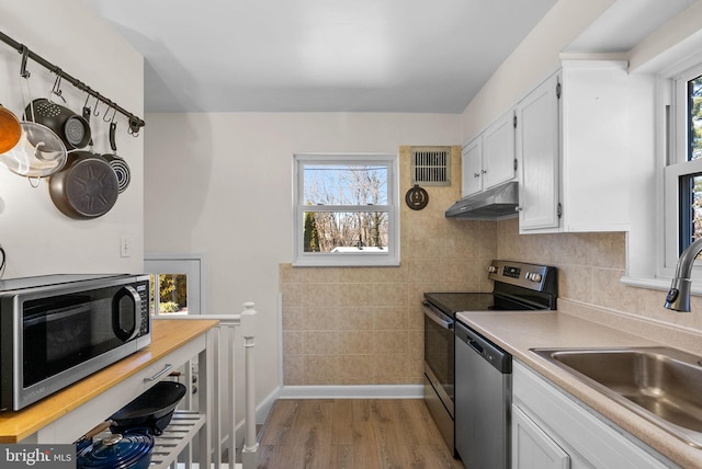 kitchen with stainless steel appliances, visible vents, white cabinetry, a sink, and under cabinet range hood