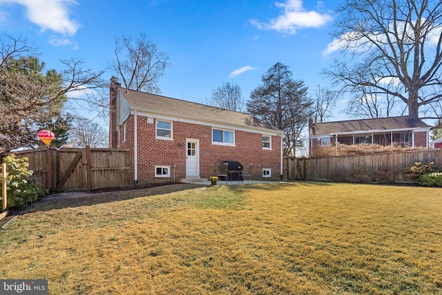 back of house with entry steps, a fenced backyard, a chimney, a yard, and brick siding