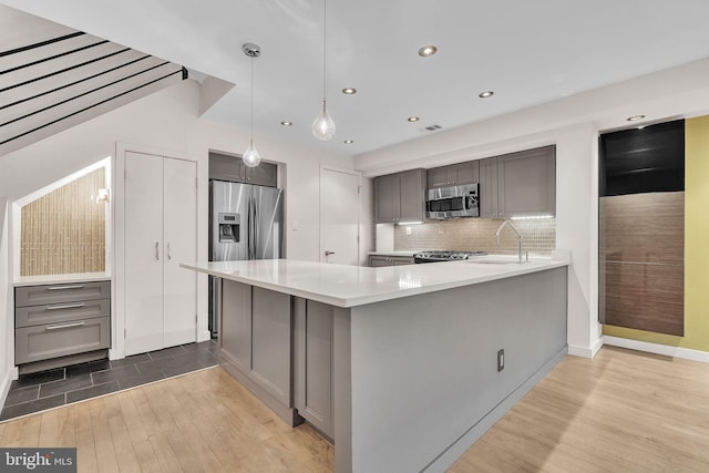 kitchen with stainless steel appliances, tasteful backsplash, gray cabinets, light countertops, and light wood-type flooring