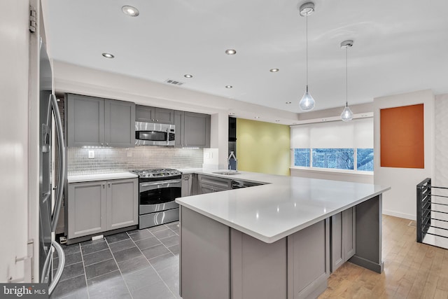 kitchen featuring gray cabinets, visible vents, appliances with stainless steel finishes, a sink, and a peninsula