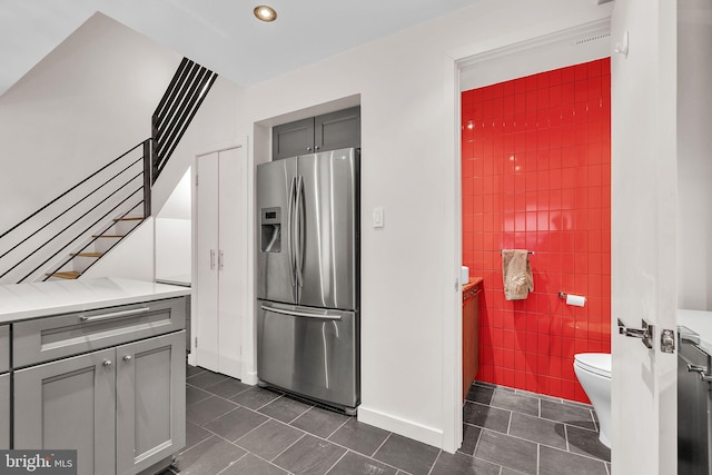 kitchen with dark tile patterned flooring, stainless steel fridge with ice dispenser, gray cabinets, light countertops, and tile walls