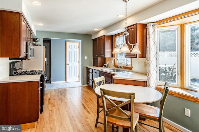 kitchen with baseboards, light wood-style flooring, a sink, light countertops, and appliances with stainless steel finishes