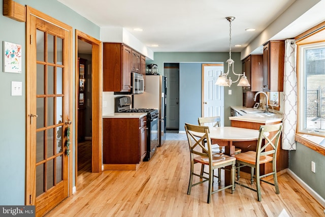 kitchen featuring light wood finished floors, stainless steel microwave, baseboards, light countertops, and black range with gas cooktop