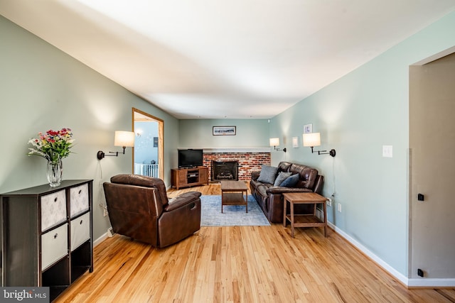 living area featuring baseboards, light wood-style floors, and a brick fireplace