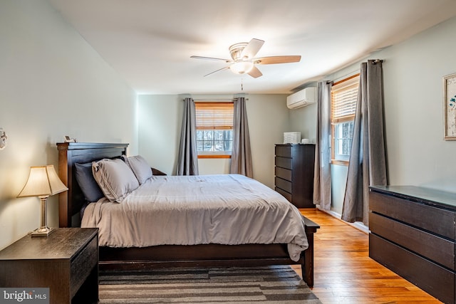 bedroom with an AC wall unit, light wood-type flooring, and ceiling fan