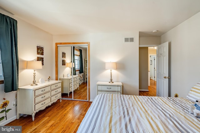 bedroom with a closet, visible vents, light wood-style flooring, and baseboards