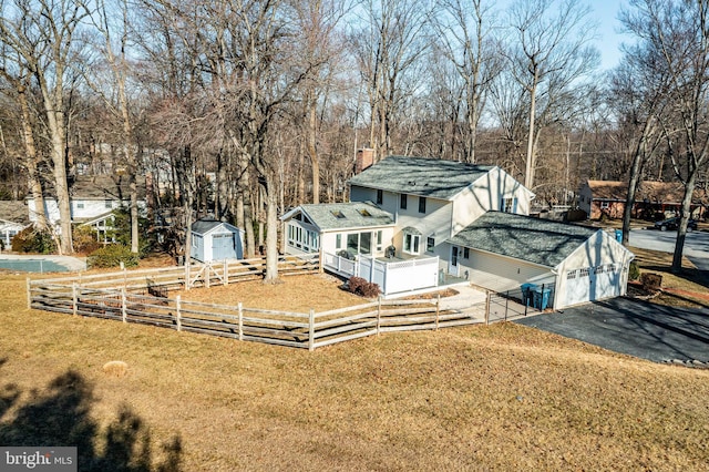 rear view of house featuring fence, a shed, a lawn, a chimney, and an outbuilding