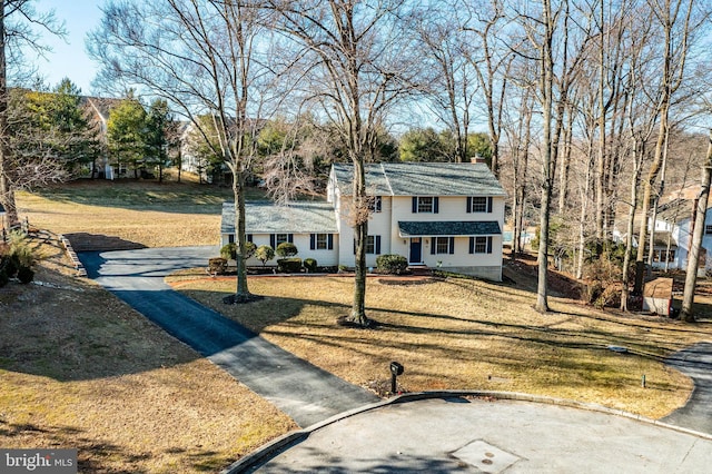 view of front facade with driveway, a chimney, and a front yard