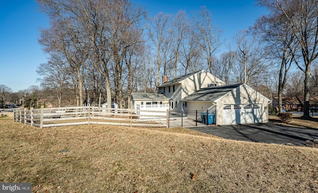 view of home's exterior featuring fence, aphalt driveway, a chimney, a yard, and an attached garage