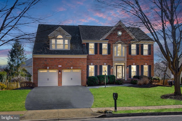 view of front facade with brick siding, a lawn, an attached garage, fence, and driveway