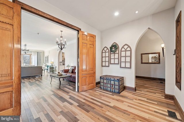 hall featuring visible vents, baseboards, arched walkways, light wood-style floors, and a notable chandelier