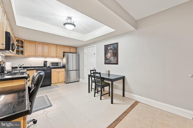 kitchen featuring a tray ceiling, black dishwasher, dark countertops, freestanding refrigerator, and baseboards