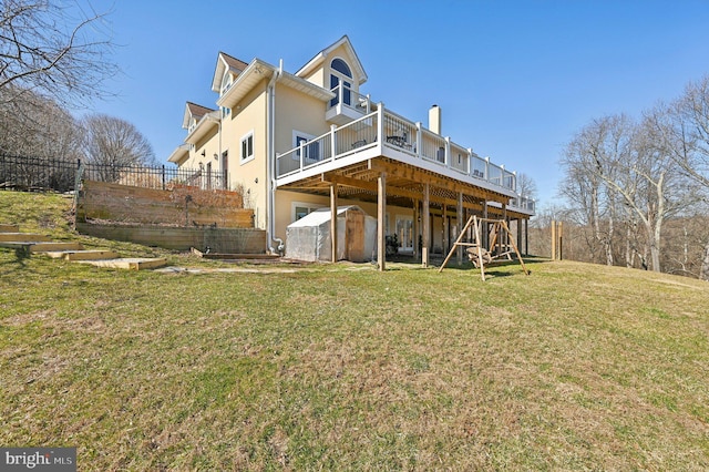 rear view of house featuring a wooden deck, a lawn, fence, and stucco siding