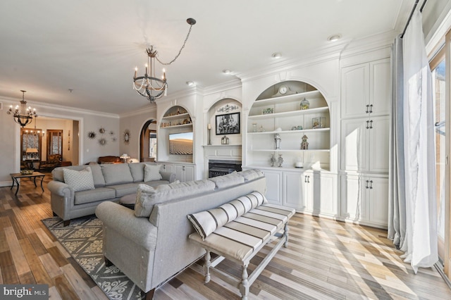 living area featuring built in shelves, arched walkways, crown molding, a notable chandelier, and light wood-type flooring