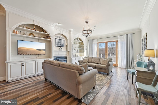 living room featuring built in features, wood finished floors, a fireplace, crown molding, and a notable chandelier