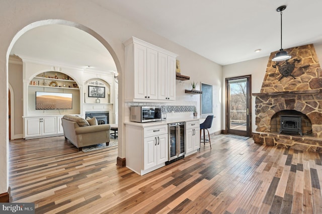 kitchen with wine cooler, stainless steel microwave, light wood-style flooring, and white cabinetry